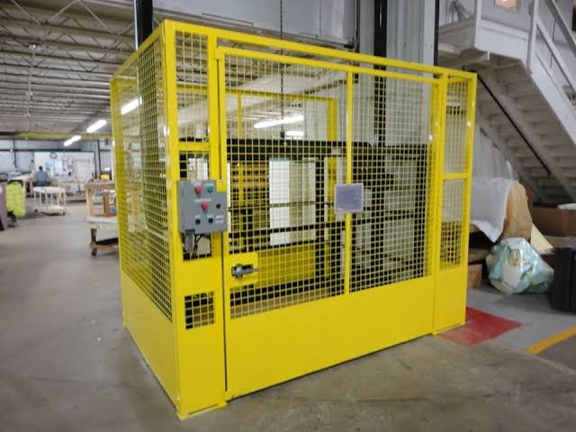 Elevador de carga industrial com estrutura amarela de proteção
