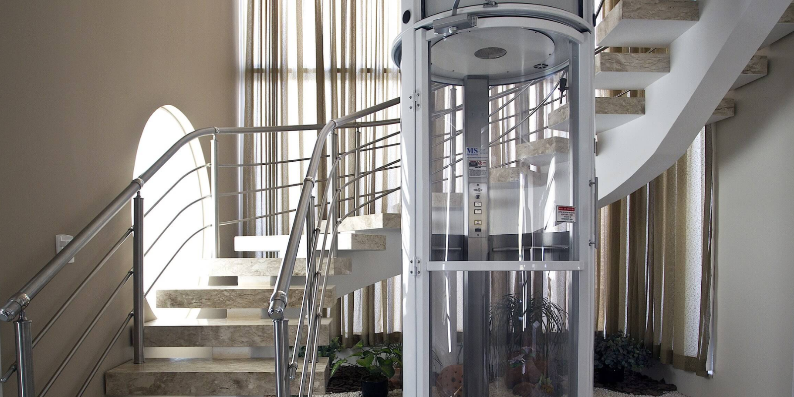 Elevador residencial panorâmico instalado ao lado de escada interna